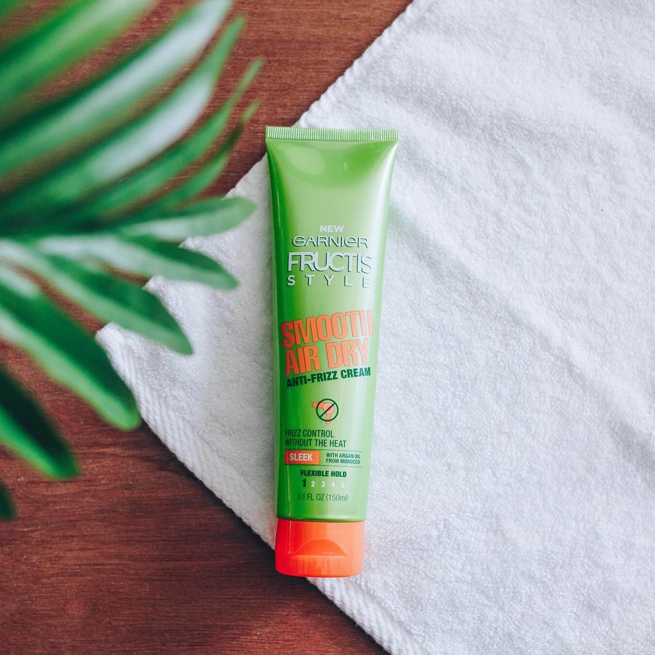 Garnier Fructis Style Smooth Air Dry Anti-Frizz Cream on a white hand towel on wood with a branch of leaves in the foreground.