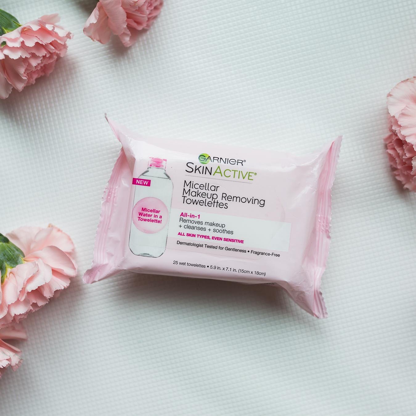Garnier SkinActive Micellar Makeup Removing Towelettes surrounded by four pink roses on a white mat.