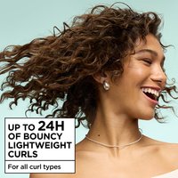 A smiling woman with bouncy, lightweight brown curls, highlighting up to 24H of curl definition for all curl types using Garnier Fructis hair products.