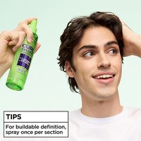 Styling tip for curly hair: man demonstrating the use of Garnier Fructis Curl Shape Defining Spray Gel by spraying once per section for buildable definition.