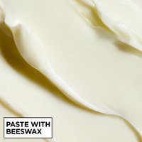 A macro close-up of thick, creamy off-white styling paste showing soft swirls and ridges, labeled "PASTE WITH BEESWAX".