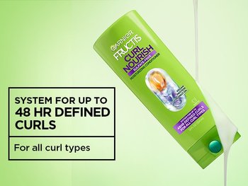 A tilted bottle of Garnier Fructis Curl Nourish Conditioner with a thick, white cream formula being squeezed out. Text on the left reads: "SYSTEM FOR UP TO 48 HR DEFINED CURLS" and "For all curl types".