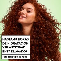 A smiling woman with long, voluminous red curly hair and freckles poses against a green background beside text reading "Up to 48H of Moisture & Bounce Between Washes, for all curl types."