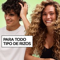 A curly-haired man running his hand through his hair smiles beside a curly-haired woman on a green background next to the text "For All Curl Types," promoting Garnier Fructis Curl Refresher.