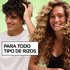 A curly-haired man running his hand through his hair smiles beside a curly-haired woman on a green background next to the text "For All Curl Types," promoting Garnier Fructis Curl Refresher.
