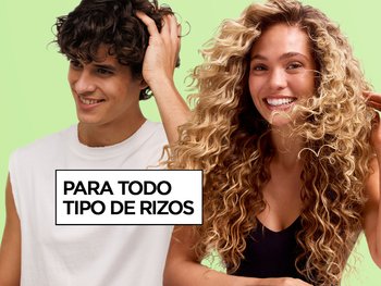 A curly-haired man running his hand through his hair smiles beside a curly-haired woman on a green background next to the text "For All Curl Types," promoting Garnier Fructis Curl Refresher.