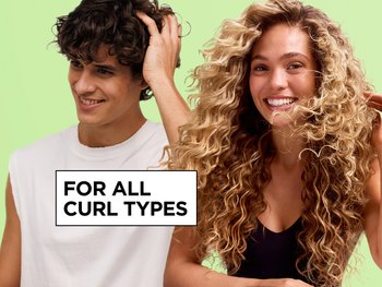 A curly-haired man running his hand through his hair smiles beside a curly-haired woman on a green background next to the text "For All Curl Types," promoting Garnier Fructis Curl Refresher.