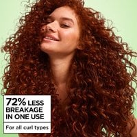 Smiling woman with voluminous, defined red curly hair against a light green background, highlighting a claim of 72% less breakage in one use for all curl types.