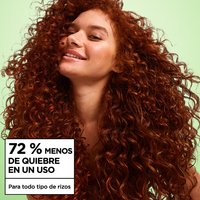 Smiling woman with voluminous, defined red curly hair against a light green background, highlighting a claim of 72% less breakage in one use for all curl types.
