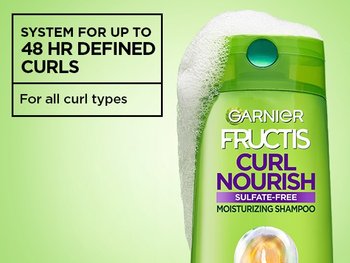 A bottle of Garnier Fructis Curl Nourish Moisturizing Shampoo with white foam on top. Text on the left reads: "SYSTEM FOR UP TO 48 HR DEFINED CURLS" and "For all curl types".