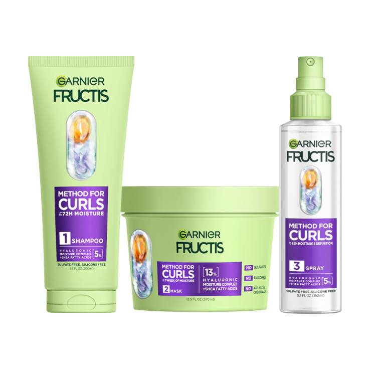 A complete set of Garnier Fructis Method for Curls products is displayed: a light green tube of “Moisture Restoring Shampoo“, a light green tub of “Defining Mask“ and a clear spray bottle of “Reviving Spray" for 48H moisture & definition and for up to 1 week of moisture. All products highlight "Hyaluronic Moisture Complex + Shea Fatty Acids."