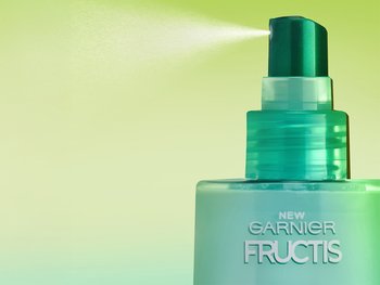A bottle of Garnier Fructis Pure Clean Detangler spritzing into the air. This milky, leave-in formula provides smooth, soft, and shiny hair with no weigh down.