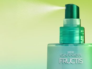 A bottle of Garnier Fructis Pure Clean Detangler spritzing into the air. This milky, leave-in formula provides smooth, soft, and shiny hair with no weigh down.