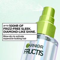 A close-up of a Garnier Fructis Diamond Sleek Shine spray bottle, actively spritzing a fine mist. Text claims "UP TO 100HR OF FRIZZ-FREE SLEEK. DIAMOND-LIKE SHINE." and instructs to "Blow-dry to activate expensive-looking hair.