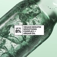 Close up shot of liquid inside a glass chemical device. Bubbles and rings are forming in an abstract way. Copy on image reads "up to 8% vegan keratin smoothing complex + argan oil".