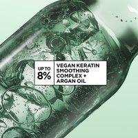 Close up shot of liquid inside a glass chemical device. Bubbles and rings are forming in an abstract way. Copy on image reads "up to 8% vegan keratin smoothing complex + argan oil".