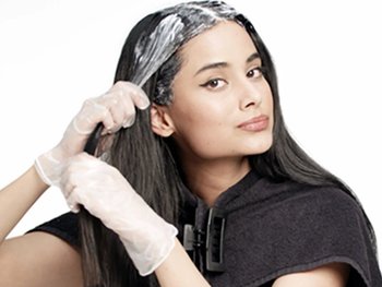 Woman with dark brown hair applying Nutrisse Ultra Color on her full head. She is applying through the lengths of her hair and massaging to evenly spread the content.