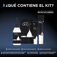 Dark black infographic graphic titled "WHAT IS IN THE KIT?" in bold white and gold text, with a small note reading "Made in a Carbon Neutral Factory." Five Garnier Olia product components are displayed in a flat-lay arrangement — including the Olia-branded tubes, powder, and developer — each labeled beneath with product names: Crème Developer, Bleaching Powder, Lightening Crème, along with Application Gloves and an Instruction Insert (text in English and Spanish noted).