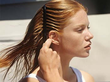 A redhead woman gently runs her fingers through her wet hair, demonstrating the use of Garnier hair care products.