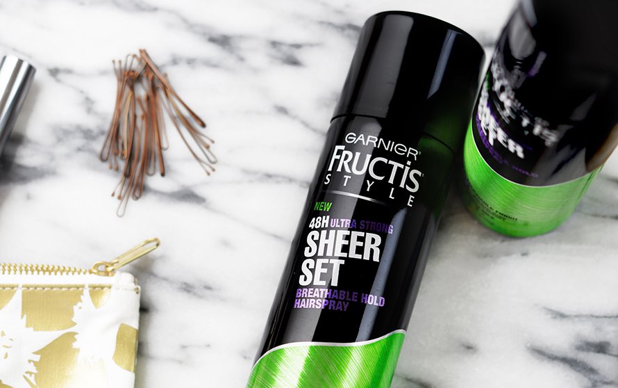 Sheer Set Ultra Strong Hold Breathable Hairspray on a black and white marble countertop with bobby pins and a gold makeup bag.