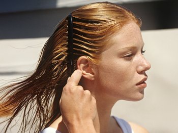 A woman with long wet hair uses a comb, illustrating one of the recommended tools for managing curly hair.