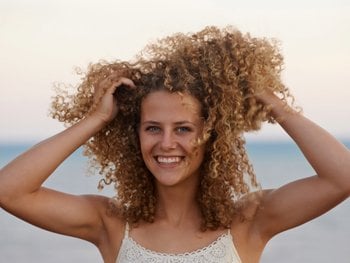 Woman holding her blonde coily hair and smiling