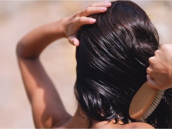 A woman with dark, glossy hair brushes her head, demonstrating the shine and health that biotin can contribute to.