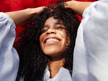 A person with curly hair is shown smiling and demonstrating improved curl definition after using argan oil.