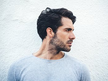 Serious portrait of a young man portraying a side part hairstyle.