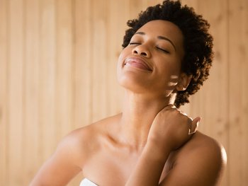 A woman tilts her head back and applies moisturizer to her neck, emphasizing the need to moisturize this delicate skin.