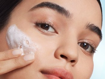 Close up of model applying foamy cleanser to her cheek.