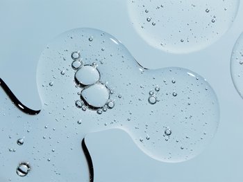 Several drops of clear cleanser on a light blue surface.