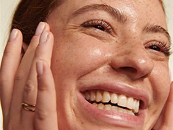 Close-up of a smiling person touching their face.